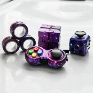 purple galaxy magnetic rings, purple galaxy infinity fidget cube, galaxy push button fidget cube, galaxy game controller on a white surface with spots of light and mirror like reflection of the magnetic rings fidget.