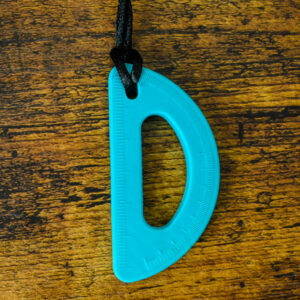 Protractor shaped chew necklace with measuring lines on the chew pendant. It's a turquoise color and on a wood table.