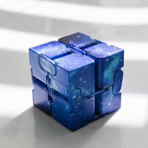 blue and light blue galaxy pattern infinity fidget cube on a thin block of light and 2 blocks of shadows on a white surface