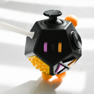 12 sided cube with buttons, gears, wheels, silicone texture side, joystick on the top in the colors pink, black, dark yellow, black.