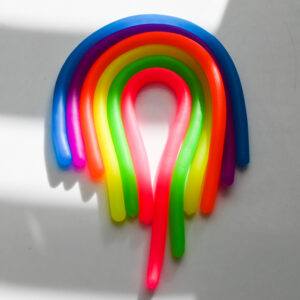 stretchy fidget noodles side by side like a rainbow and a thick block of light shining on the middle, and the top is in a block of shadow with light above it. There's a slight vintage film haze.