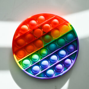 rainbow colored circle shape with push bubbles. It's on a white surface with blocks of light and shadows shining down on it.