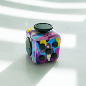 painting print made from pink, light blue, white, pink, yellow fidget with buttons, turn wheel, joystick, switches.