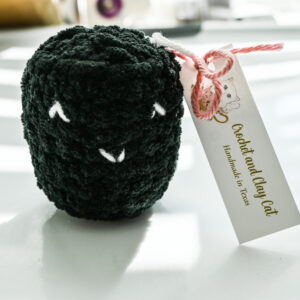 smiling black crocheted squishy with Crochet and Clay Cat's tag attached