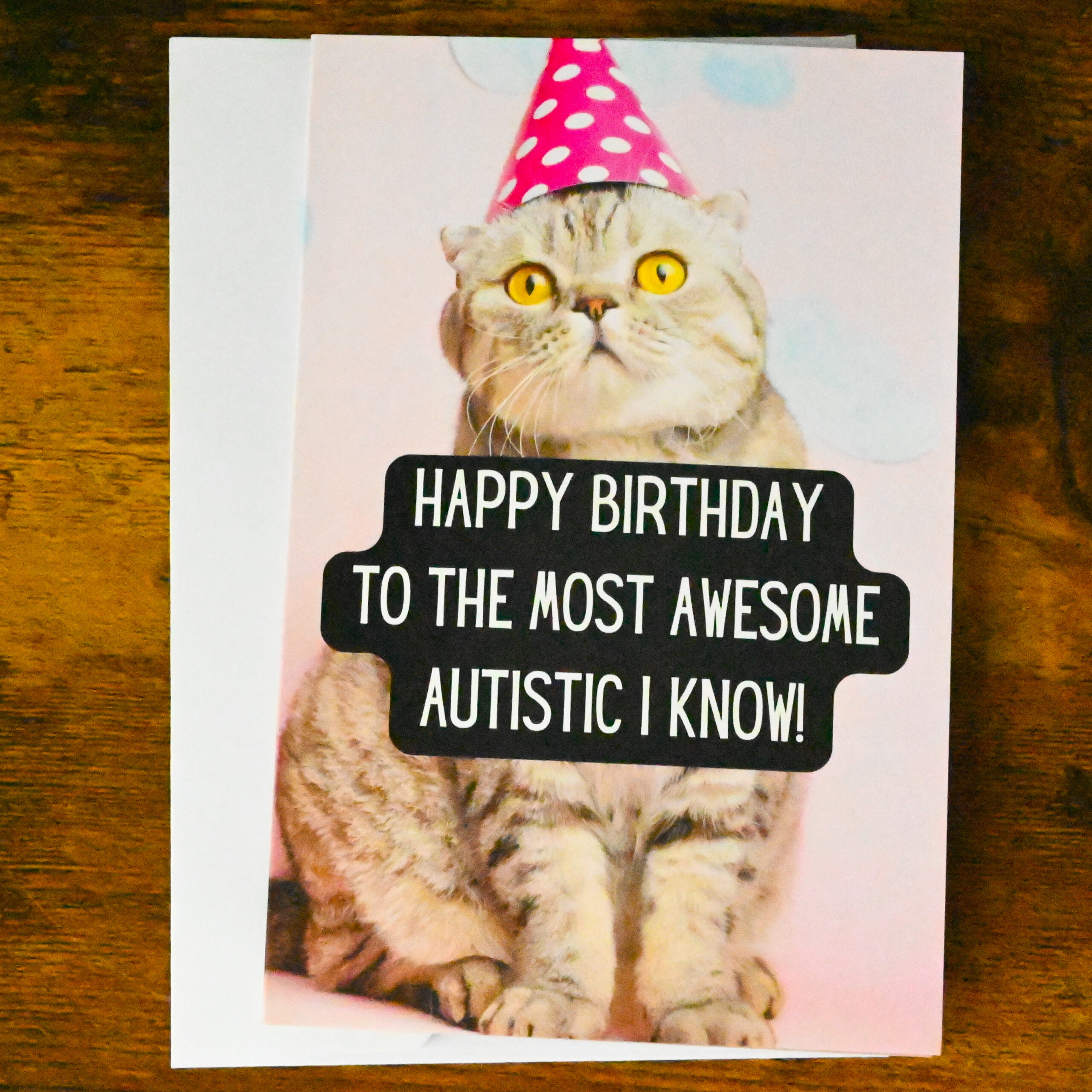 Pink background with blue clouds and a cat wearing a pink polka dot party hat. Text says "Happy Birthday to the Most Awesome Autistic I Know"