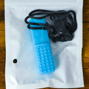 blue bar chew necklace inside the plastic bag packaging with the necklace string wrapped around the very top of the pendant