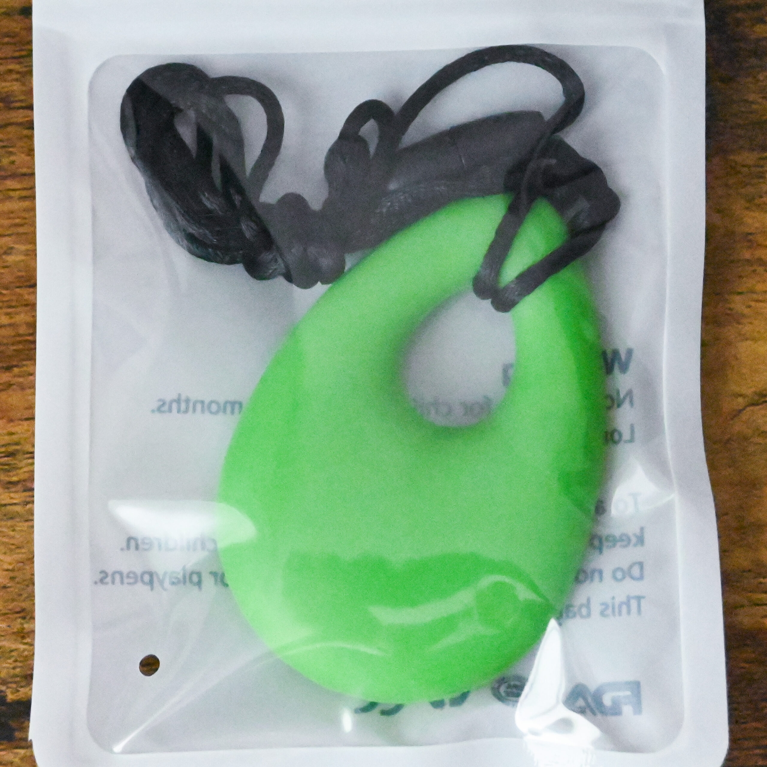 green teardrop chew pendant inside the bag packaging on a wood table