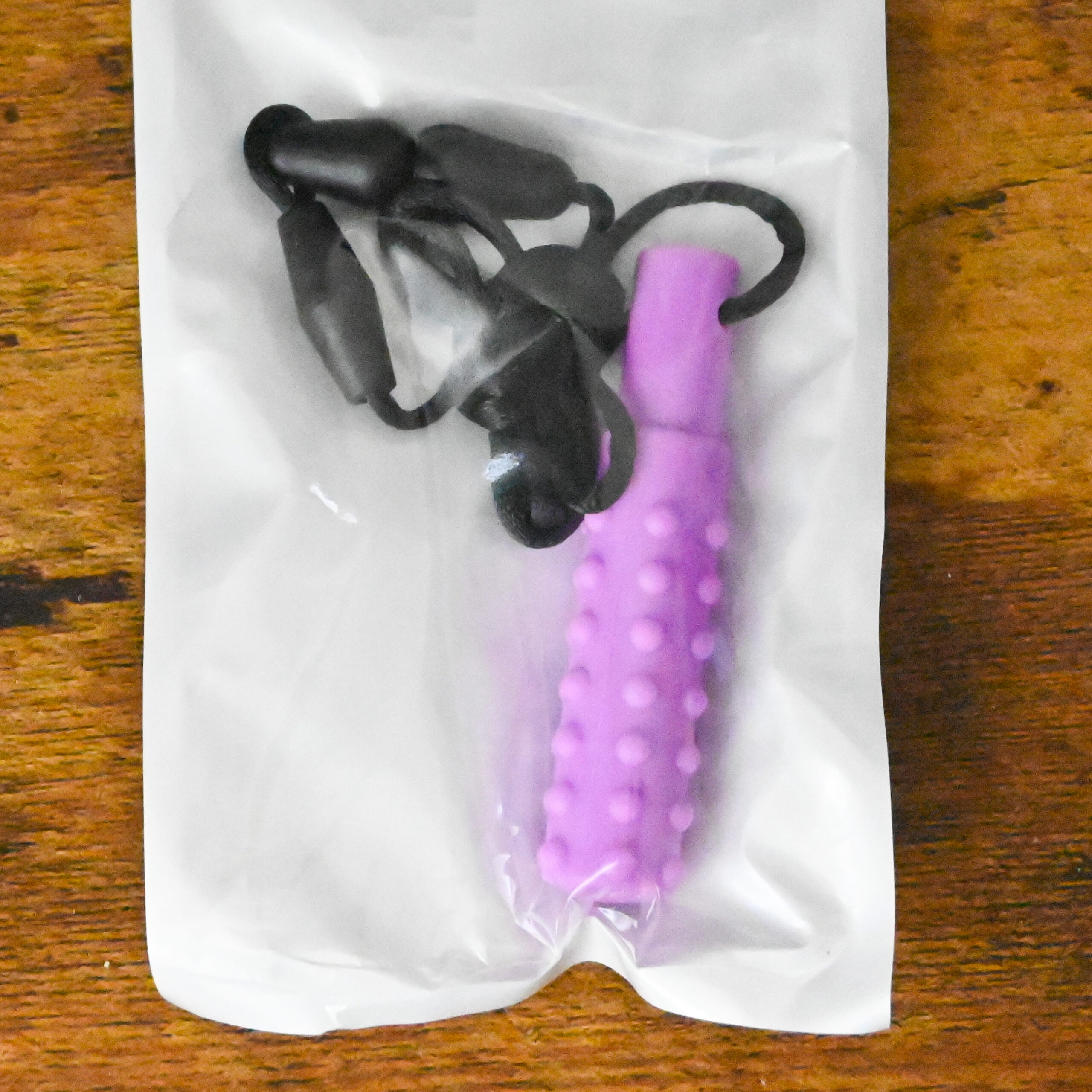 purple textured chew necklace inside the bag packaging and on a wood table