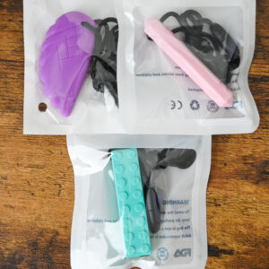 purple feather chew necklace, pink prism pendant chew necklace, and a turquoise block chew necklace shaped like a building block toy.